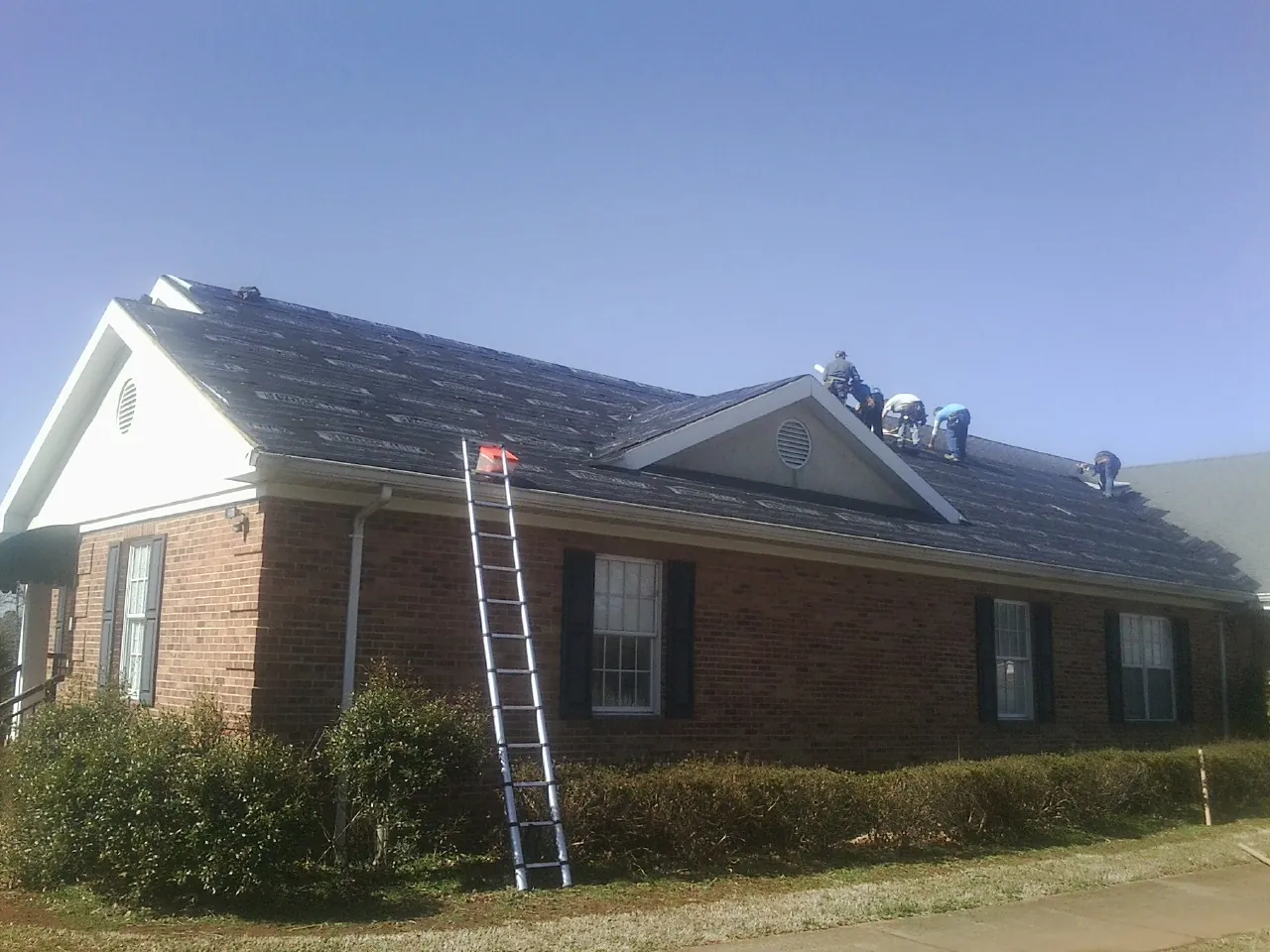 Crew tearing shingles off a brick ranch roof with a ladder set — Emergency Roof Repair work by our crew in Mossville
