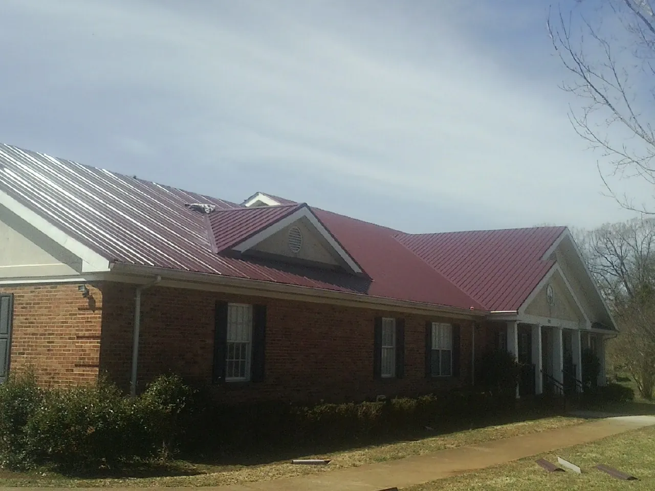 Red metal roof with gabled entries on a long brick building, from a Hail Damage Roof Repair job in Mossville