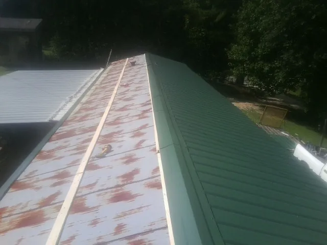 Old rusted panels beside newly installed green metal roofing — Wind Damage Roof Repair by Roofing Brothers in Mossville