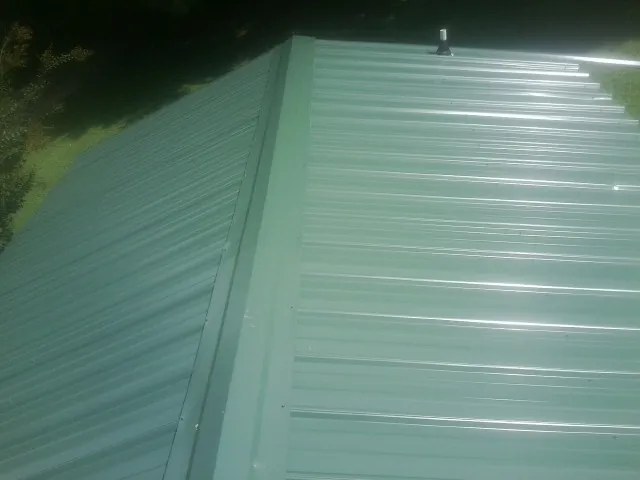 New green metal panels meeting at the ridge of a roof — Flat Roof Repair work by our crew in Mossville