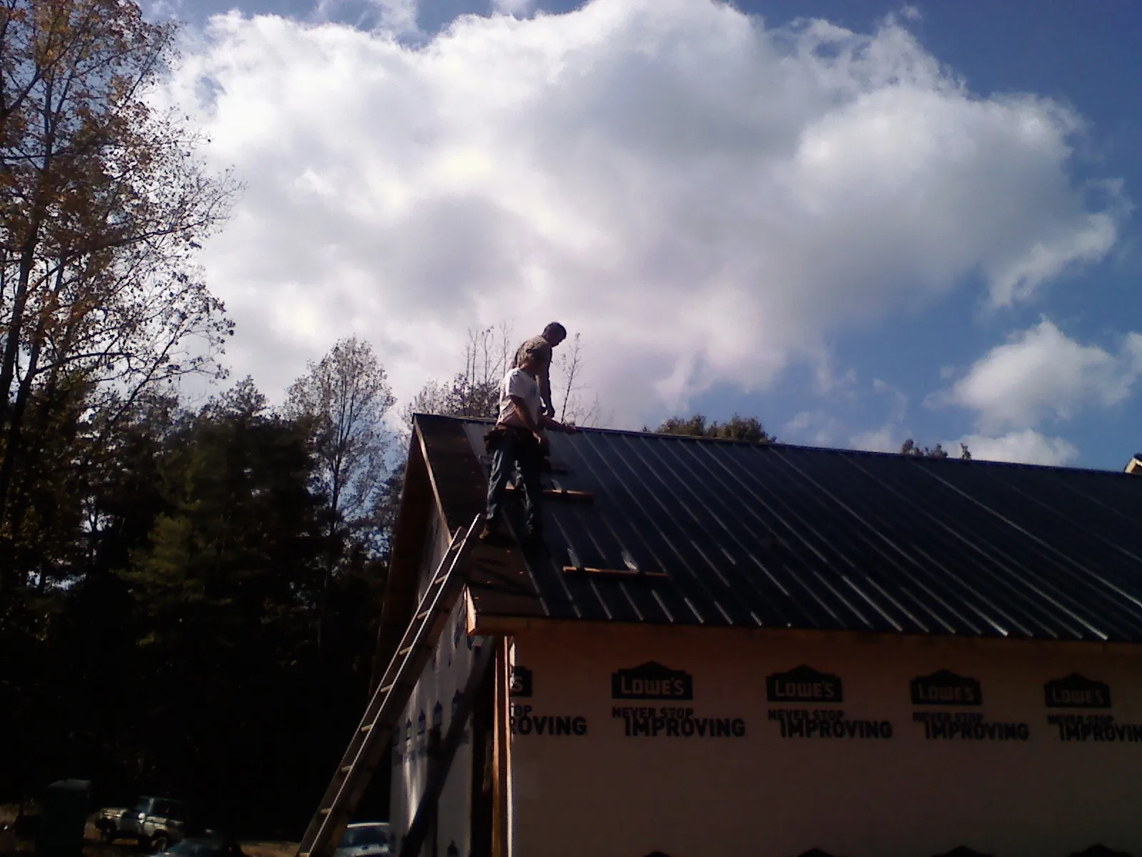 Roofer fastening dark metal panels high against a cloudy sky, from a Roof Inspection job in Mossville