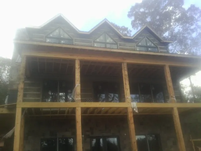 Dormers and porch framing on a large log home under construction — Roof Coating work by our crew in Mossville