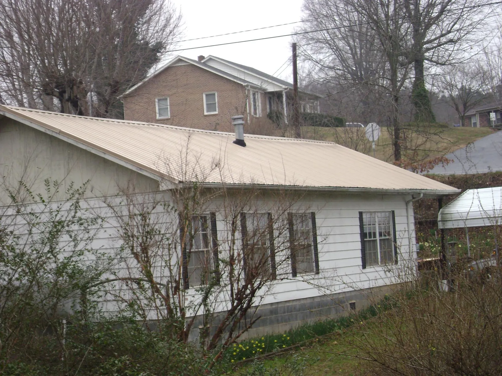 Tan metal roof on a white sided house set into a hillside — Commercial Roofing by Roofing Brothers in Mossville