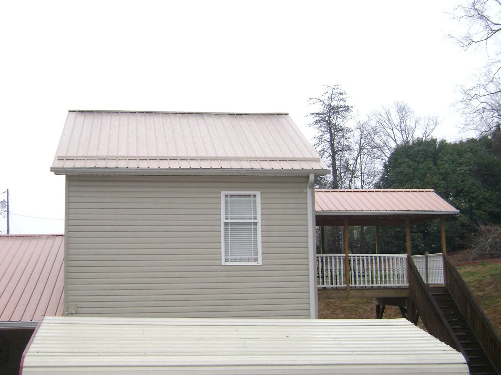 Tan metal roofs on a two story addition and attached porch, from a Roof Replacement job in Mossville